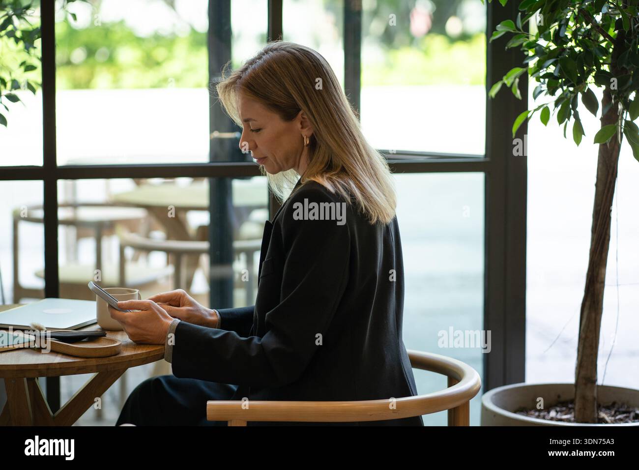 Entspannte Geschäftsfrau mit Smartphone, während sie in der Mittagspause von der Arbeit am Kaffeetisch sitzt. Stockfoto