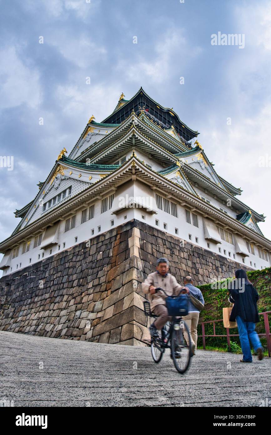 Osaka, Japan - 4. November 2025: Motion Blur Japanischer Mann fährt mit dem Fahrrad bergab in der Nähe des Schlosses Osaka mit einem Paar-Hintergrund Stockfoto