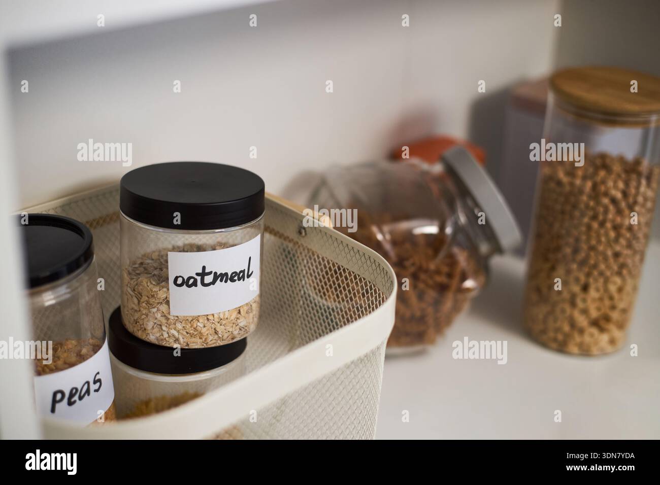 Glasgläser mit Haferflocken, Erbsen und Getreide stehen und liegen auf Küchenregalen, transparente Behälter mit Kennzeichnung für die Aufbewahrung von Lebensmitteln, Trockenwaren in Speisekammer Stockfoto