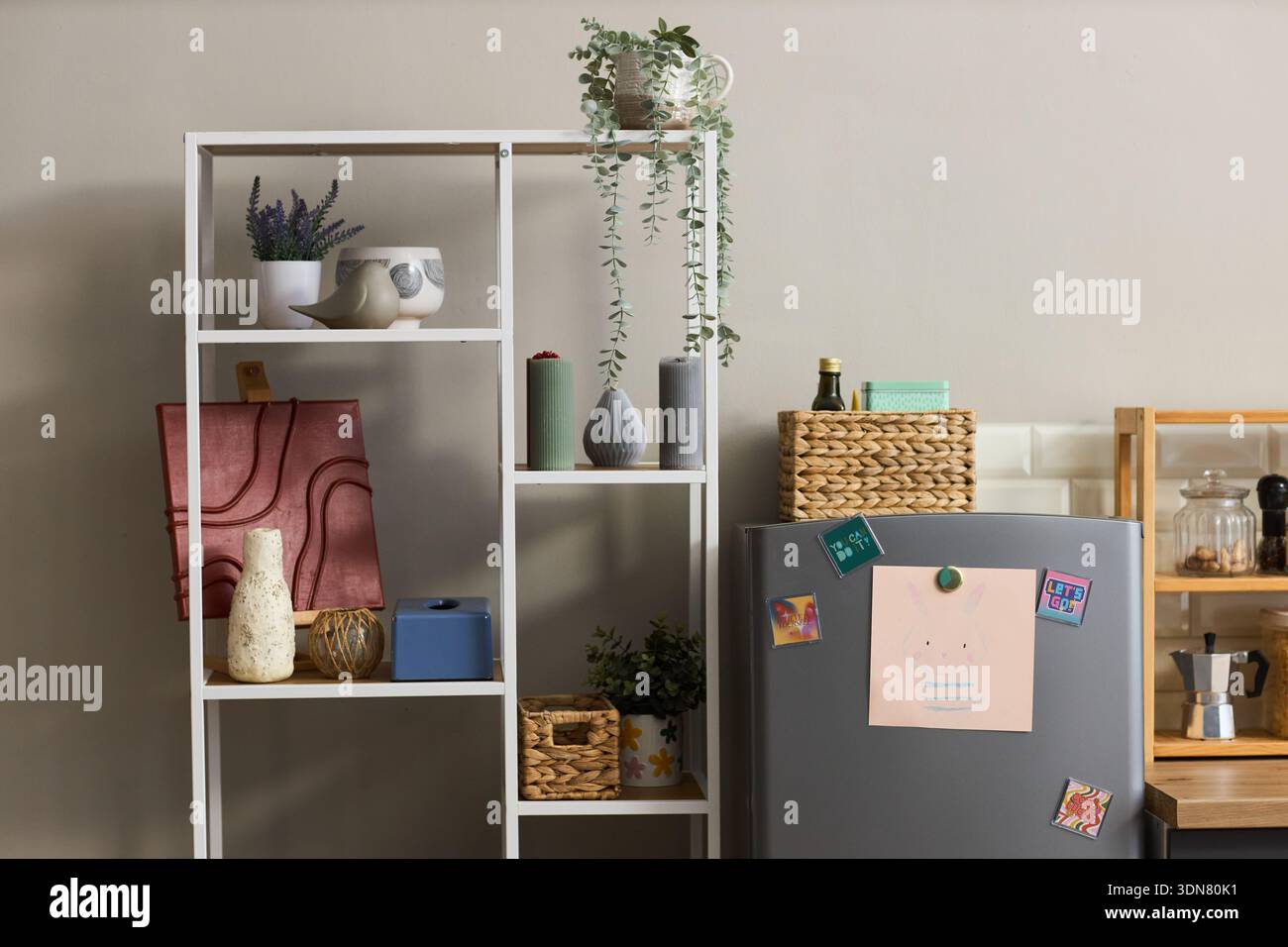 Moderne Kücheneinrichtung mit Metallregal mit dekorativen Vasen, Topfpflanzen, Lagerkörben und Kühlschrank mit Magneten und Kinderzeichnung an der Tür Stockfoto