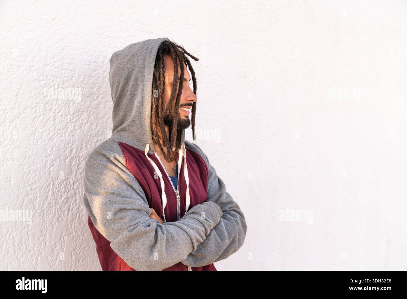 Junger Mann mit Dreadlocks und einem Hoodie im Profil, der vor einer weißen Wand steht Stockfoto