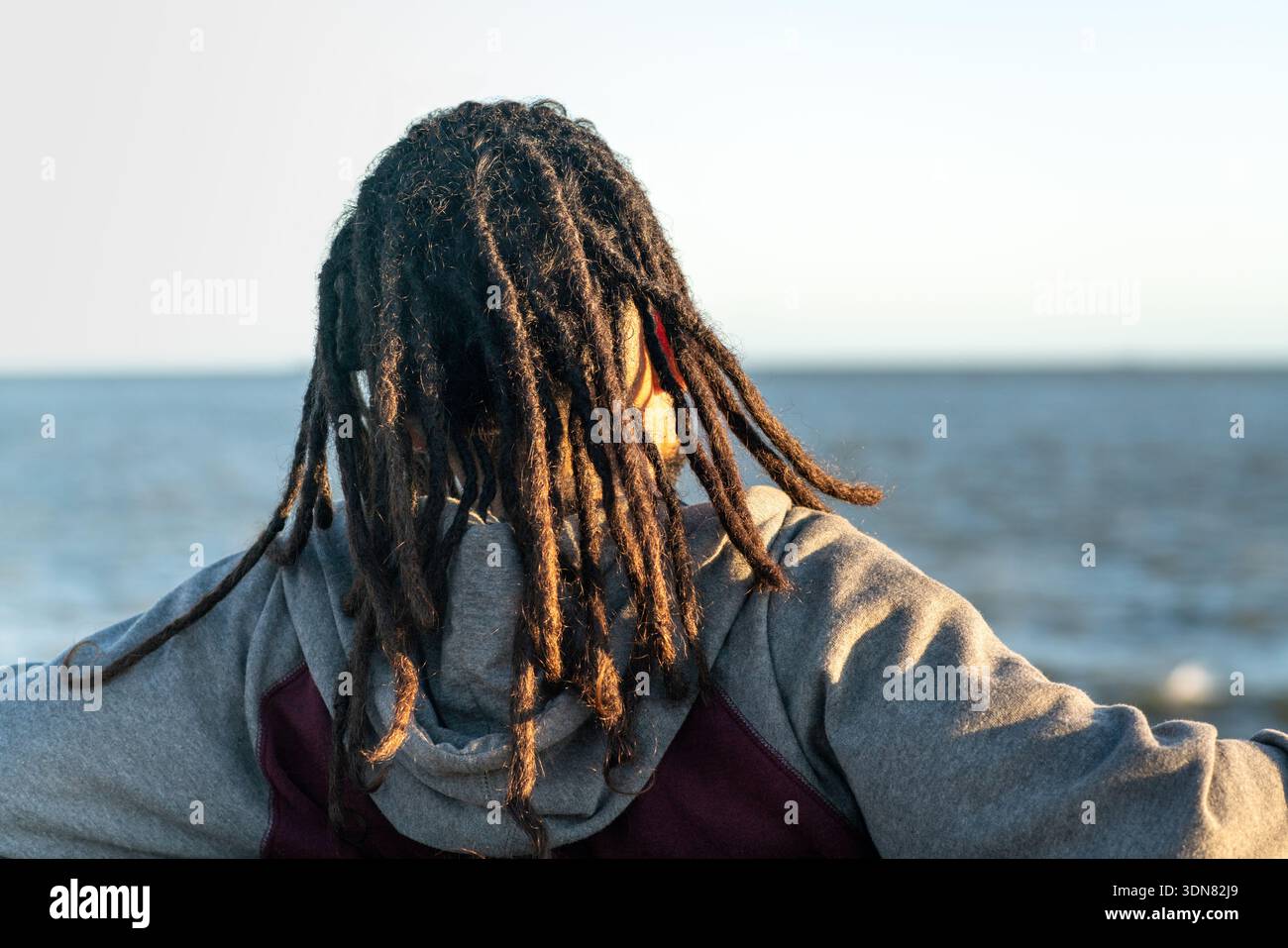 Person mit Dreadlocks mit Blick auf den Ozeanhorizont während eines Sommersonnenuntergangs Stockfoto