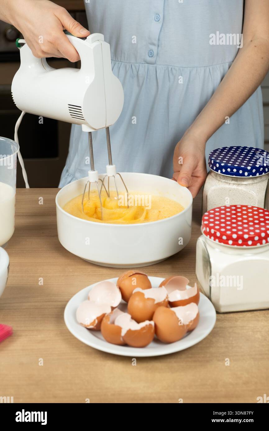 Frau, die einen elektrischen Handmixer benutzt, um Eier für Waffeln oder Kuchen zu peitschen Stockfoto