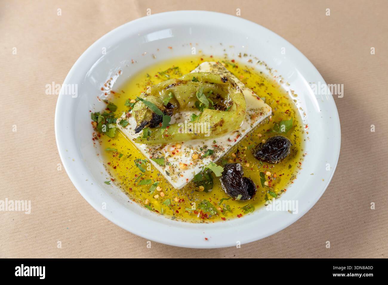Griechische Vorspeise mit einem Block erstklassigen Feta-Käse, getränkt in extra nativem Olivenöl und aromatischem Oregano, gekrönt mit einem rauchig gerösteten grünen pe Stockfoto