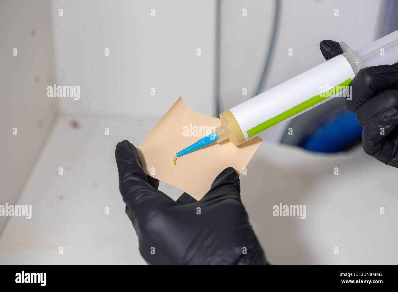 Nahaufnahme einer Hand mit Handschuhen, die einen professionellen Insektizid-Gelköder von einer Applikatorspritze auf ein kleines Stück Papier für Hausschädlinge abgibt Stockfoto