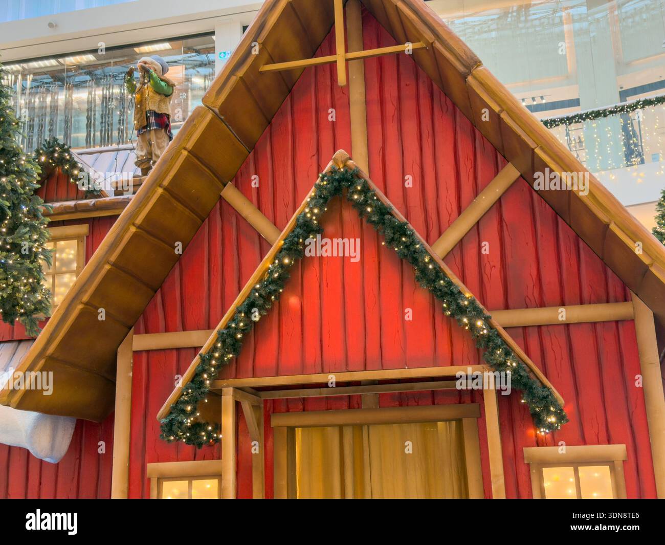Nahaufnahme einer bezaubernden roten Holzhausdekoration mit glitzernden Girlanden und einer skurrilen Figur auf dem schneebedeckten Dach, die den festlichen Einkauf unterstreicht Stockfoto