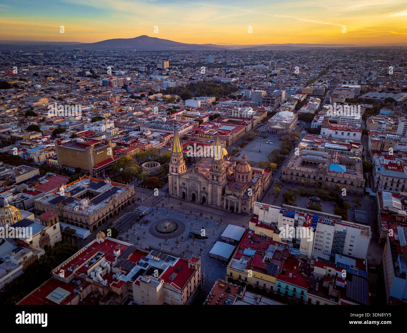 Blick auf den Sonnenaufgang aus der Luft auf die Innenstadt von Guadalajara, Jalisco, mit der Metropolitan Cathedral, den Plätzen, der Kolonialarchitektur und der weiten Skyline der Stadt mit Stockfoto