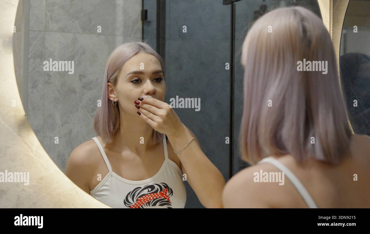 Eine junge Frau, die im Spiegel im Badezimmer schaut Stockfoto