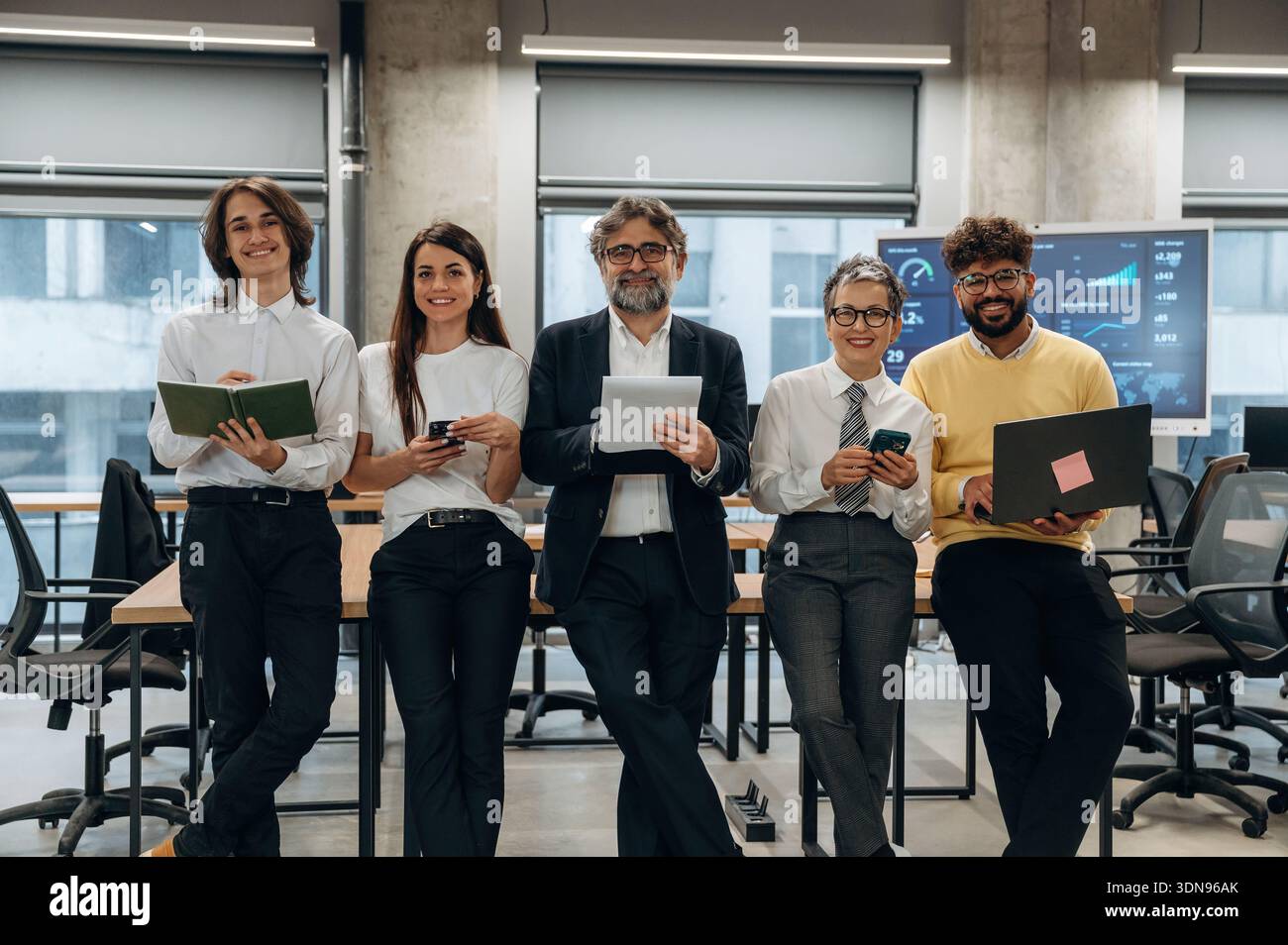 Eine Vielzahl von Geschäftsleuten steht selbstbewusst in einem modernen Büro, das Teamwork und Zusammenarbeit mit eleganten Möbeln und Technol präsentiert Stockfoto