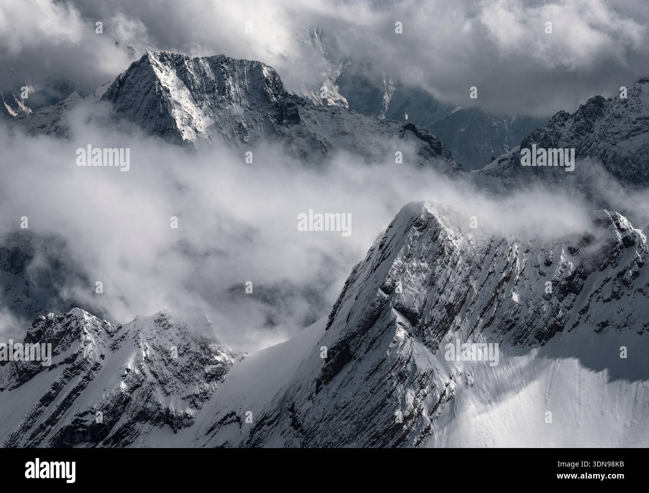 Dunkelblaue, dramatische Berggipfel, die durch Wolken und Nebel in einer stimmungsvollen alpinen Landschaft auftauchen. Stockfoto