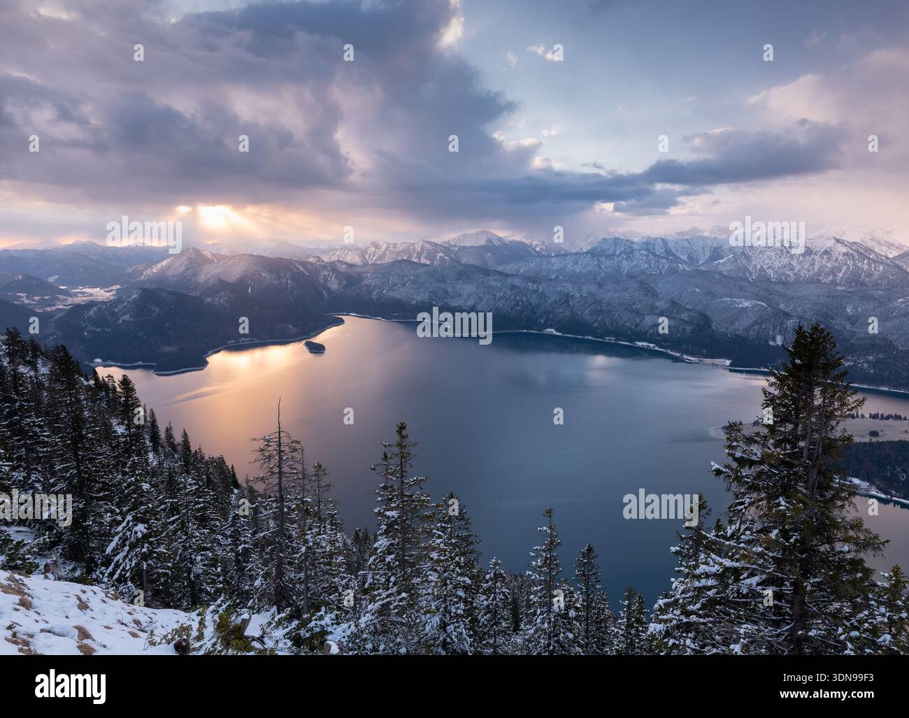 Wintersonnenaufgang mit Pastellfarben am Himmel über dem Walchensee mit den schneebedeckten zerklüfteten Bergen im Hintergrund. Stockfoto