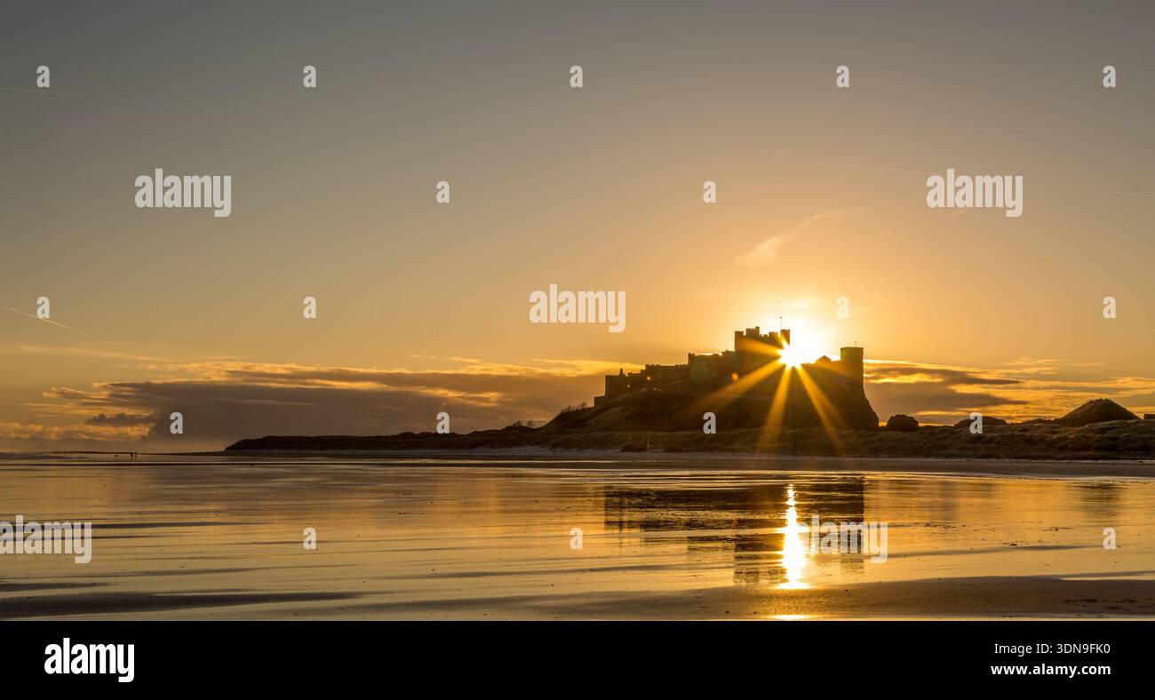 Das berühmte Bamburgh Castle an einem eiskalten Morgen bei Sonnenaufgang, neben dem schneebedeckten Strand in Northumberland, England. Stockfoto