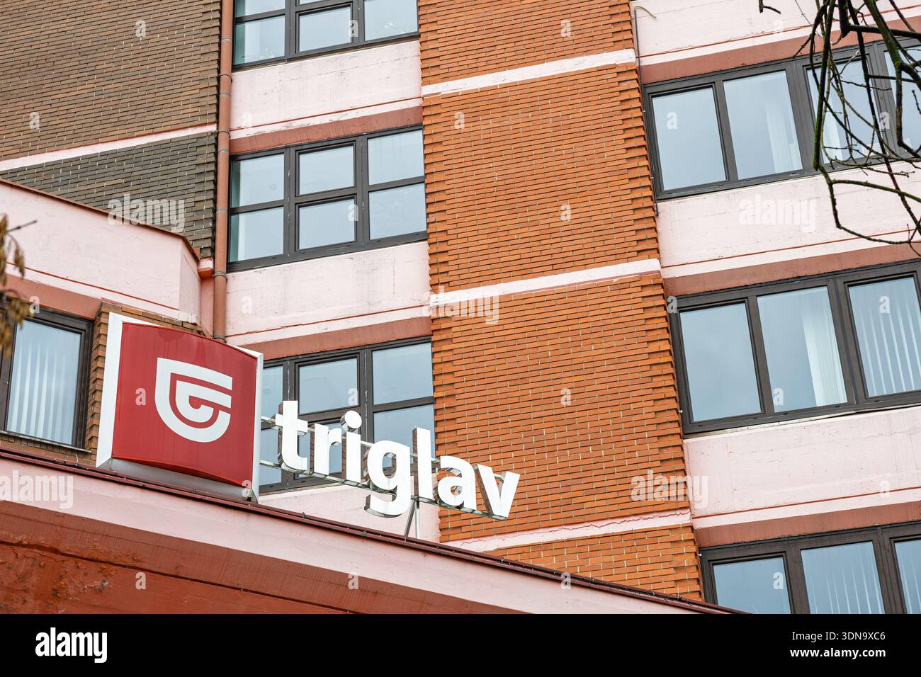 CELJE, SLOWENIEN, 01.03.2026: Fassade eines Backsteingebäudes mit rotem Triglav-Schild und markantem weißem Logo, mit mehreren rechteckigen Fenstern. Urban corp Stockfoto