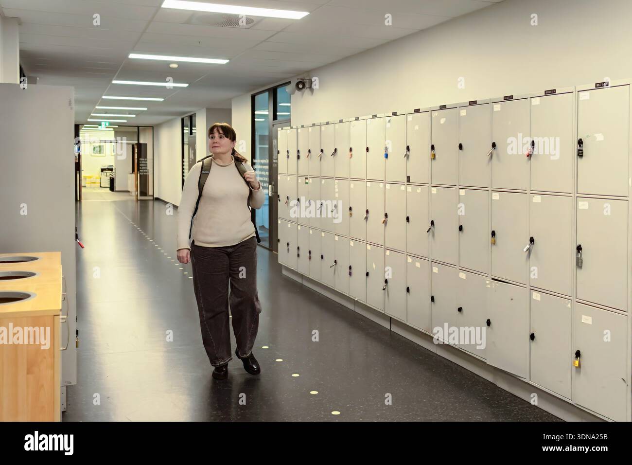Weibliche Individuen gehen in einem geräumigen Flur, der mit Schließfächern gesäumt ist, lässig gekleidet, was eine entspannte Atmosphäre in einer modernen Anlage schafft Stockfoto