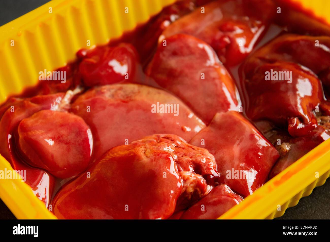 Rohe Hühnerleber in einem gelben Supermarkttablett, auf grauem Tischhintergrund Stockfoto