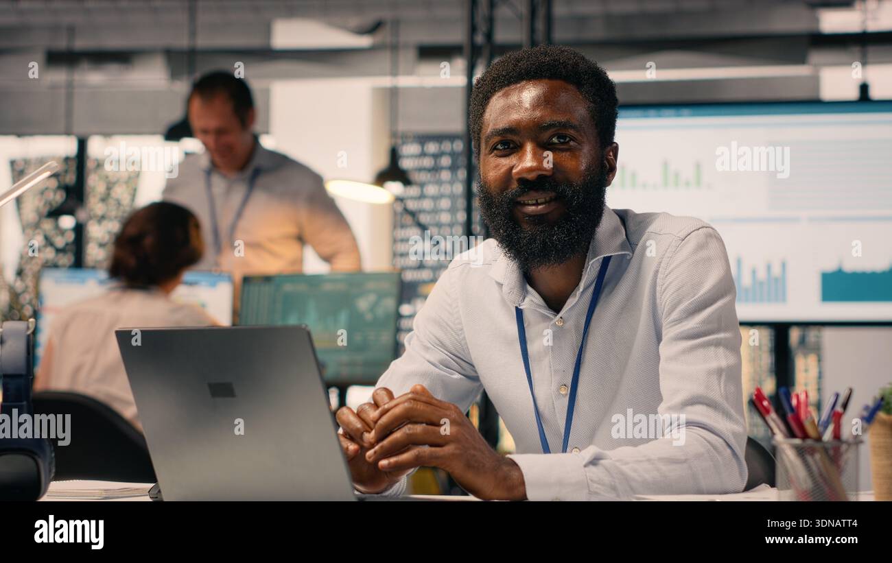 Porträt eines schwarzen Mitarbeiters, der Aufgaben auf einem Laptop für den Unternehmenserfolg löst und Leistungsbeurteilungen mit KPI- und Gelddaten durchführt. Produktivität und Unternehmensstil im Büro. Stockfoto