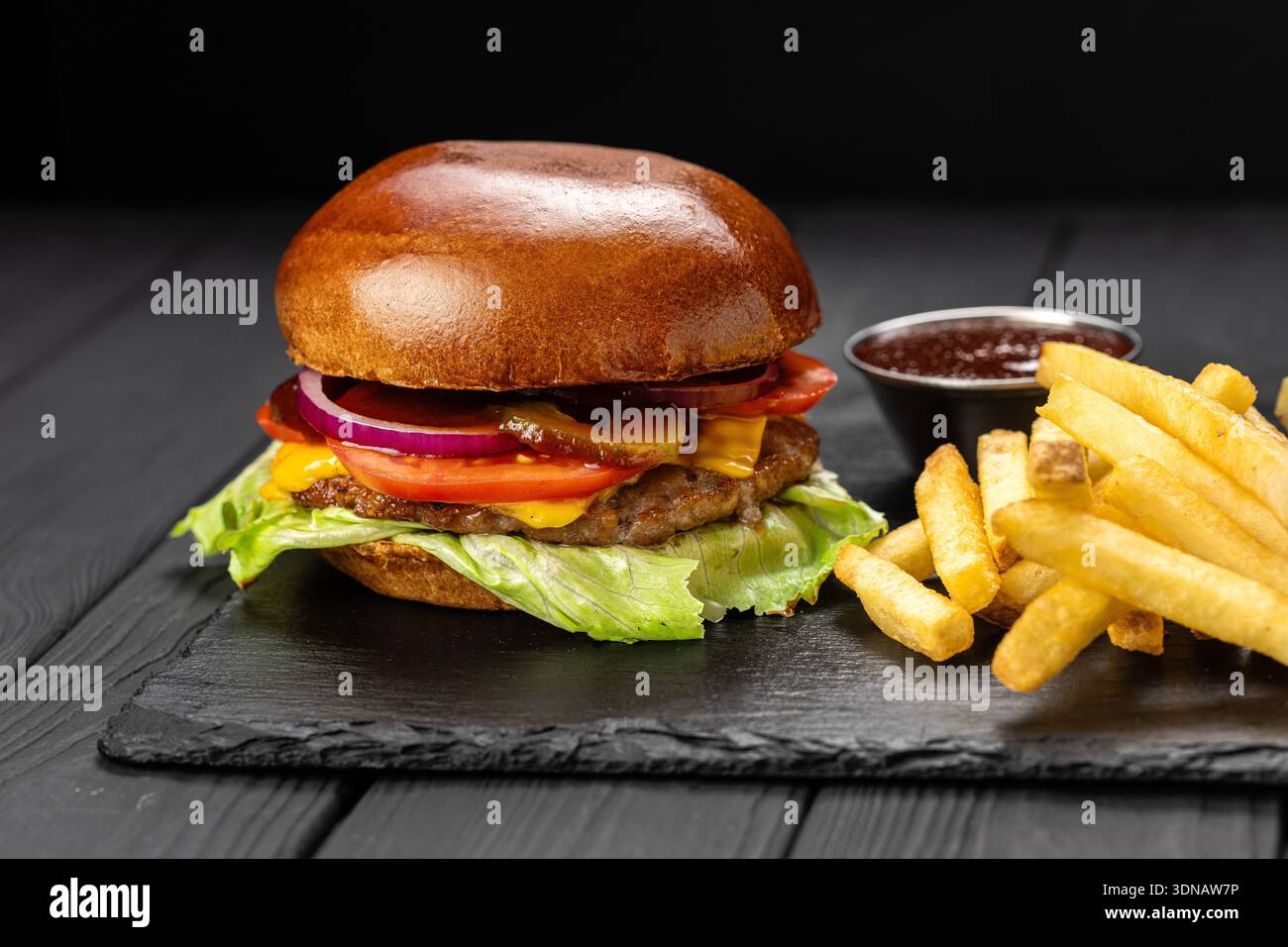 Rindfleisch-Cheeseburger mit Salat, Tomaten und Zwiebeln, serviert mit Pommes und Ketchup auf Schieferbrett Stockfoto