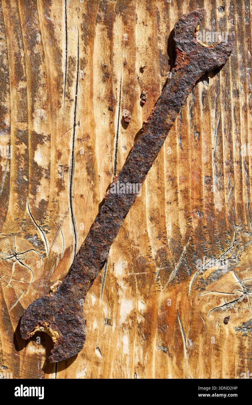Ein stark verrosteter Schraubenschlüssel, der auf einem dickem Holz liegt, mit tiefer Körnung und Kratzern. Stockfoto