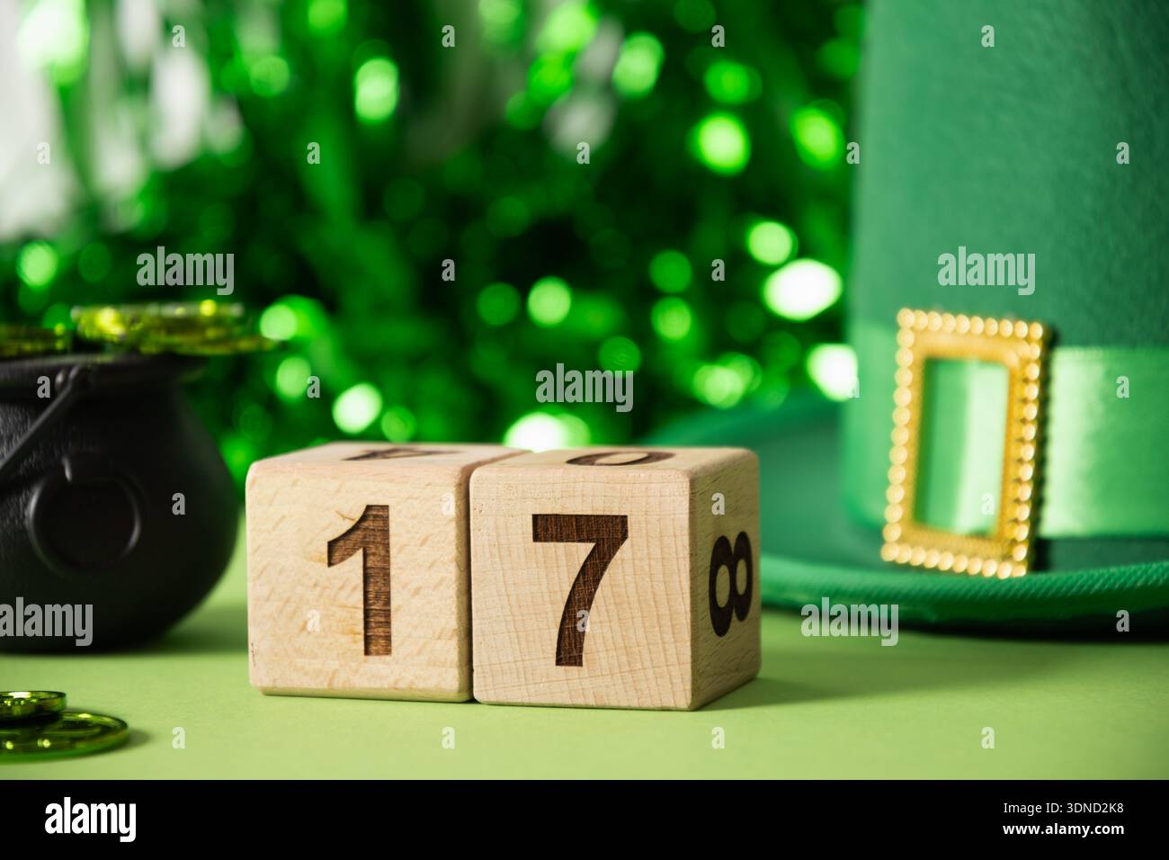 Komposition zum St. Patricks Day mit hölzernen Kalenderblöcken mit der Zahl 17, grünem Hut, Münzen und festlichen Dekorationen auf grünem Hintergrund. Stockfoto