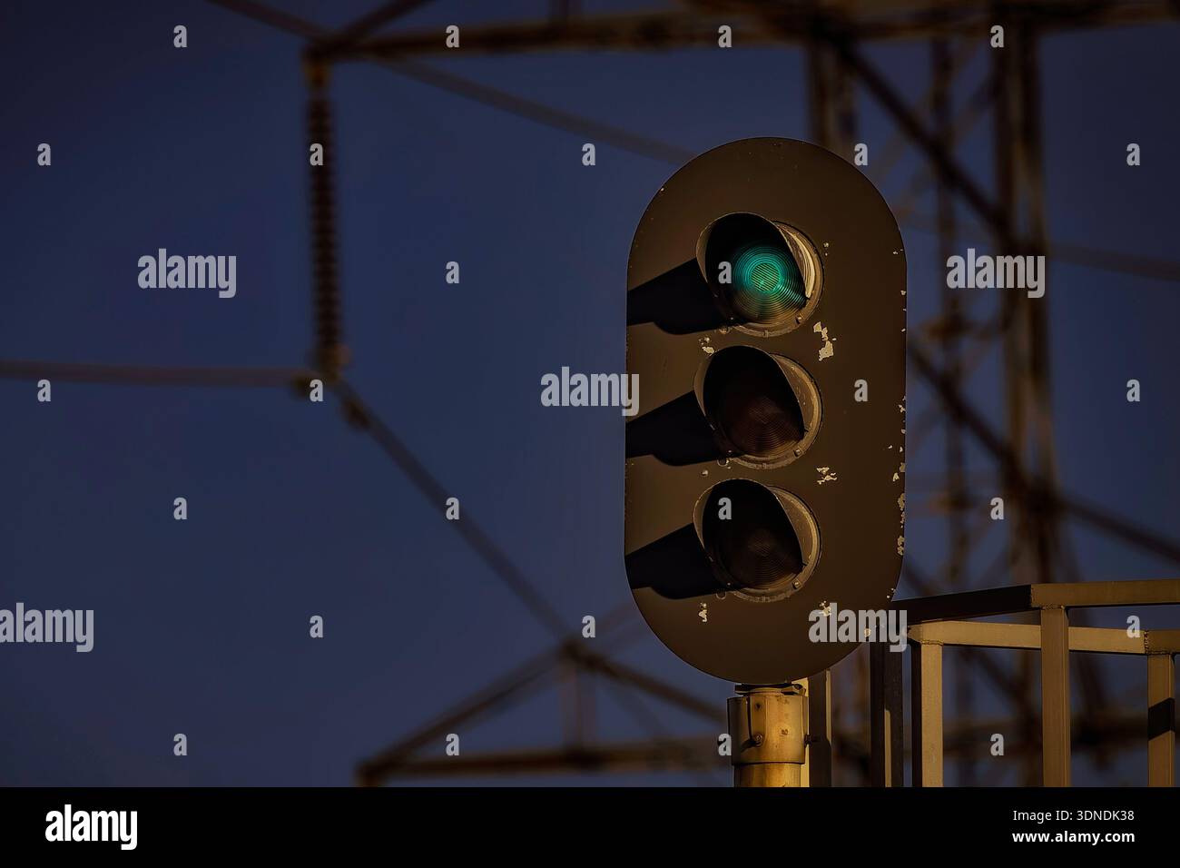 Grünes Eisenbahnsignal, das in der Abenddämmerung leuchtet, mit Silhouetten im Hintergrund. Stockfoto