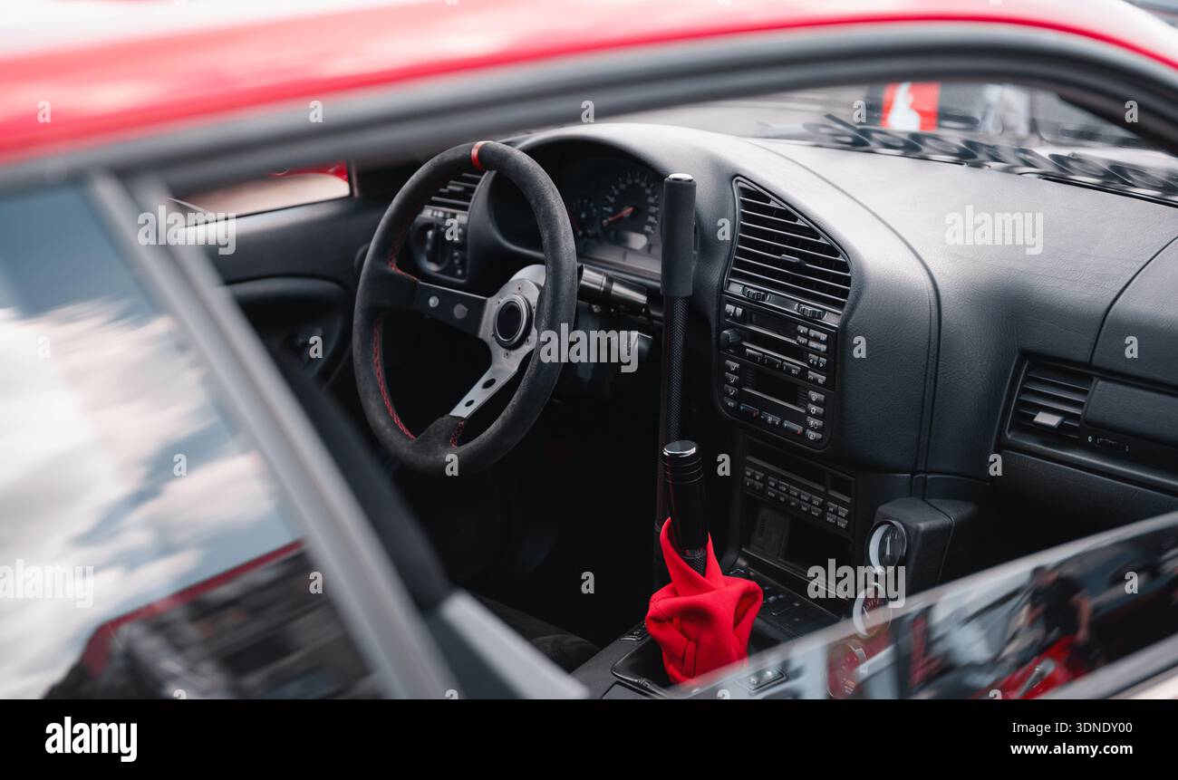 Alte rote Sportwagen-Innenausstattung. Dunkler Innenraum eines modifizierten Sportwagens aus den 1990er Jahren mit Rennlenkrad und langem Handbremshebel. Stockfoto
