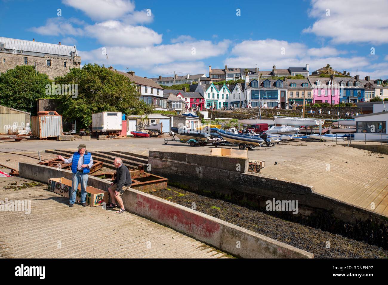 Männer sprechen im Hafen von Baltimore mit farbenfrohen Gebäuden am Wasser in Baltimore, County Cork, Irland. Stockfoto
