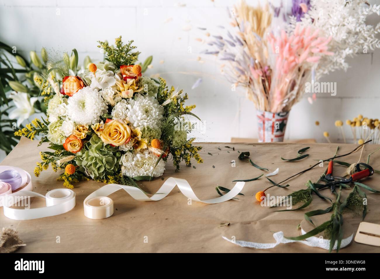 Blumenstrauß mit Rosen und Chrysanthemen auf braunem Papier neben Bandrollen. Nachhaltiges Blumengeschäft, plastikfreie Geschenkverpackung Stockfoto