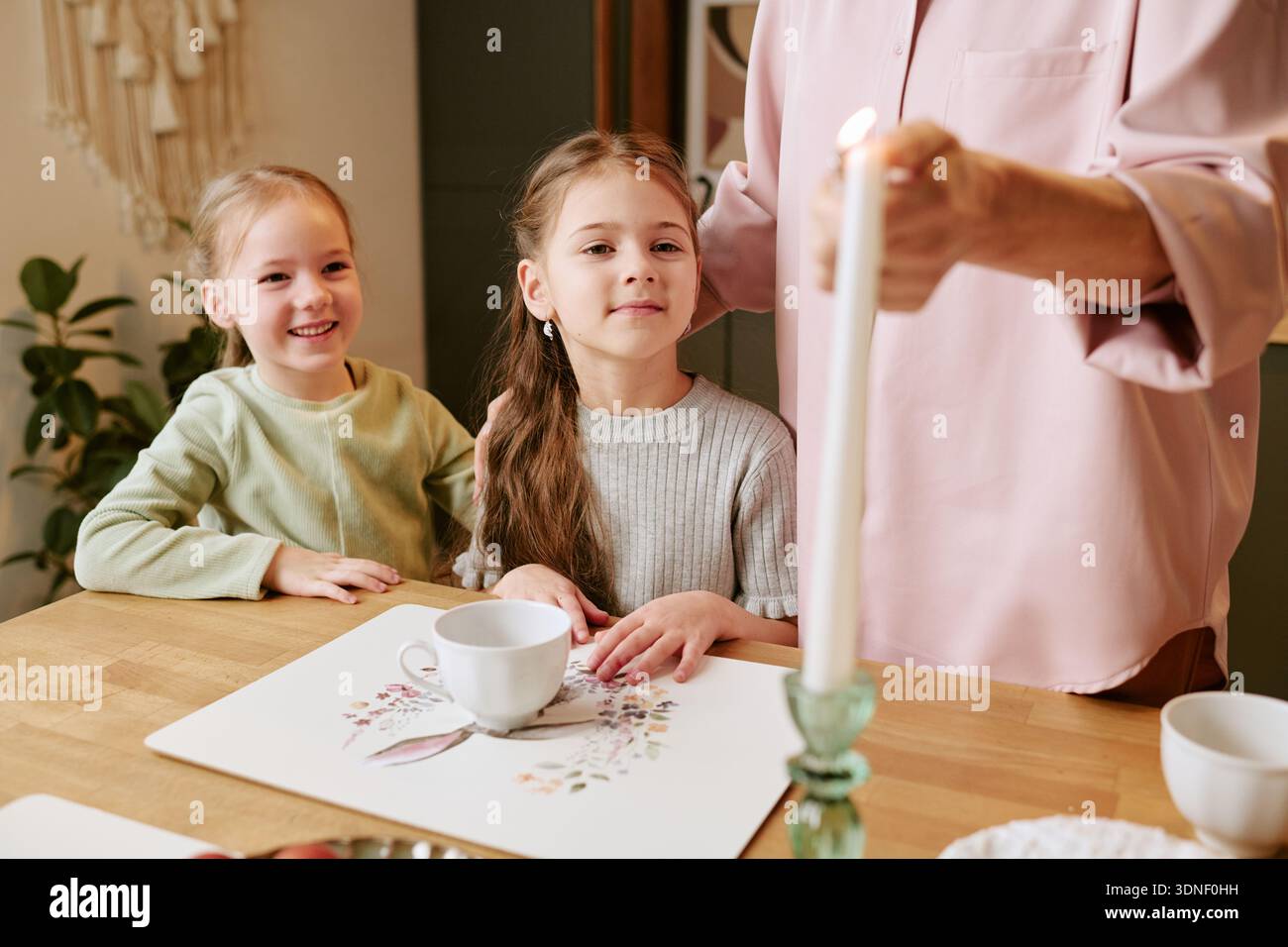 Zwei Mädchen lächeln, während sie mit Kerze für Erwachsene am Tisch sitzen Stockfoto