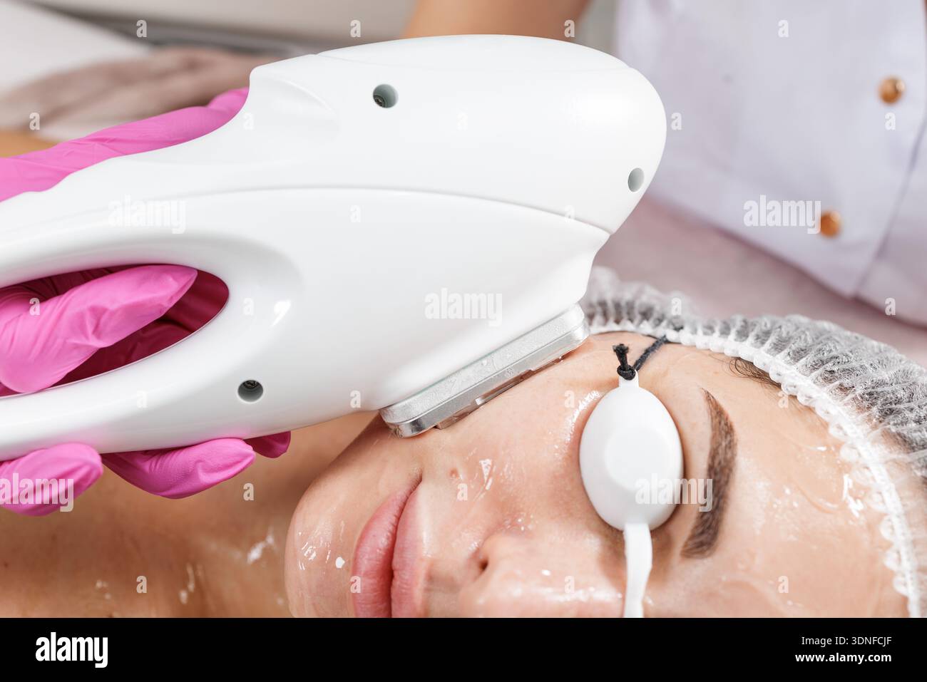 Kosmetikerin führt IPL-Verfahren mit intensivem gepulstem Licht an weiblicher Klientin mit einem Lichtgerät durch. Ideal für Dermatologie, ästhetische Medizin und fortgeschrittene Patienten Stockfoto
