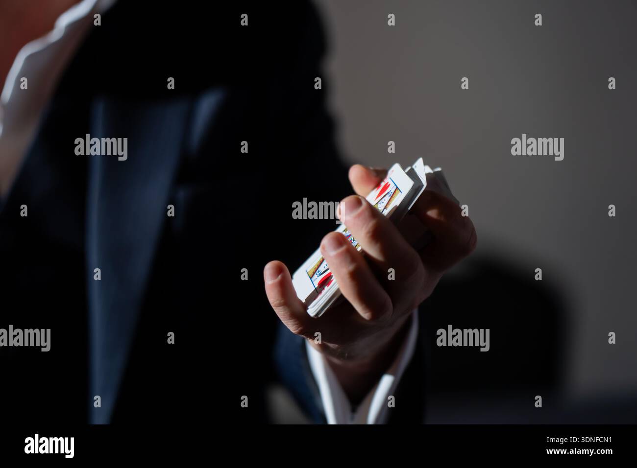 Zauberhand, die einen Stapel Spielkarten bei schlechten Lichtverhältnissen hält, einen flachen Fokus auf den Fingern und farbenfrohe Kartenränder mit dunklem Kopierraum im Hintergrund für Myster Stockfoto