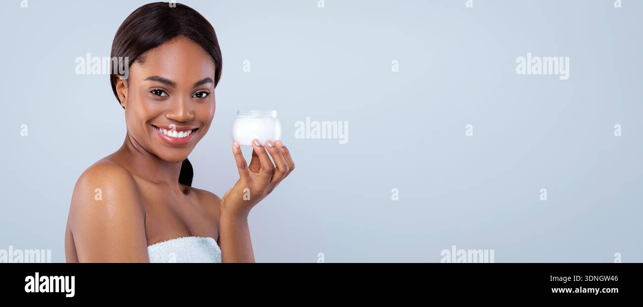 Frau hält Creme Container und lächelt im Plain Hintergrund Stockfoto