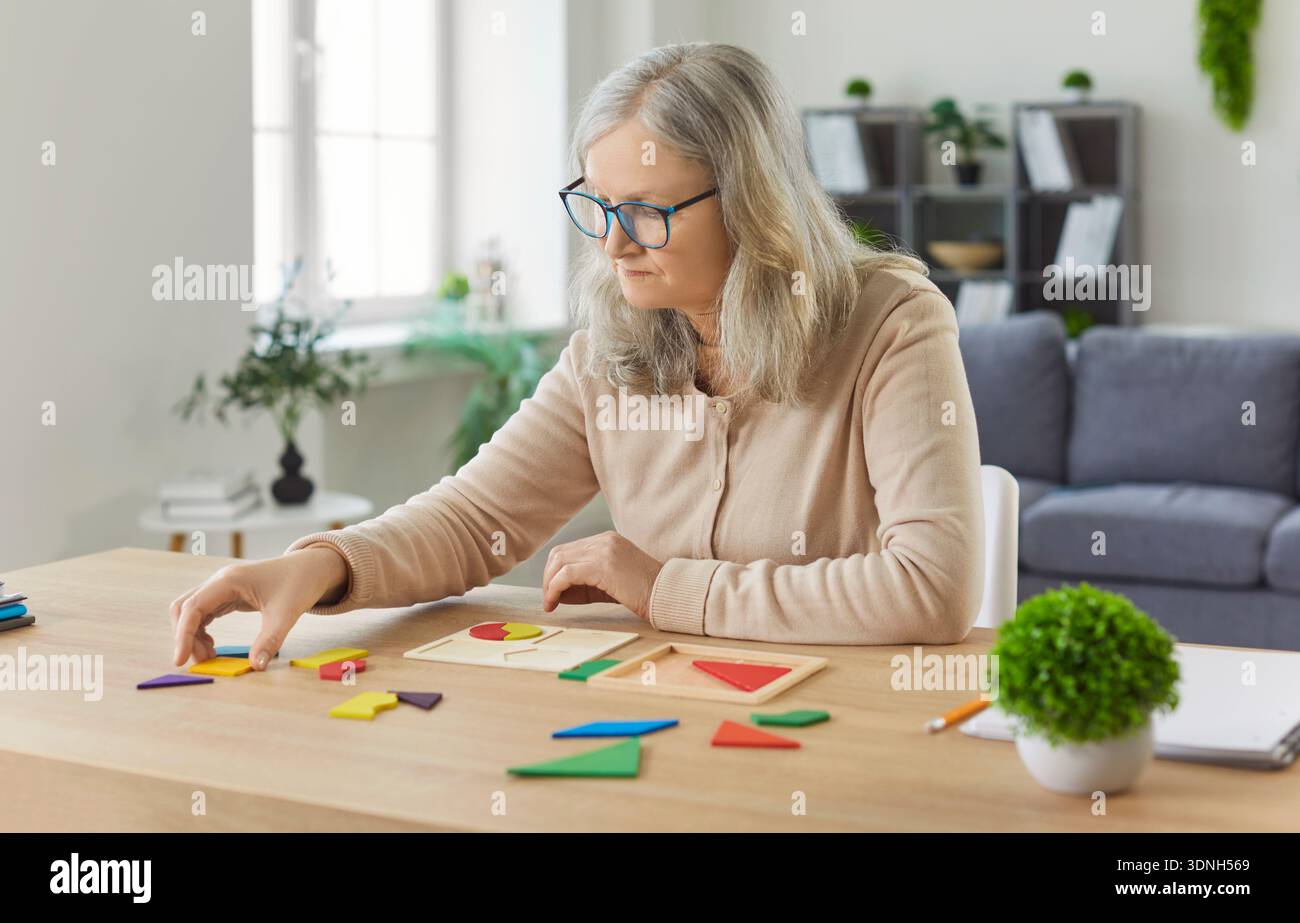Seniorin, die an geometrischen Puzzle-Spielen arbeitet, das Spiel aufnimmt, arrangiert, fokussiert auf Training Stockfoto