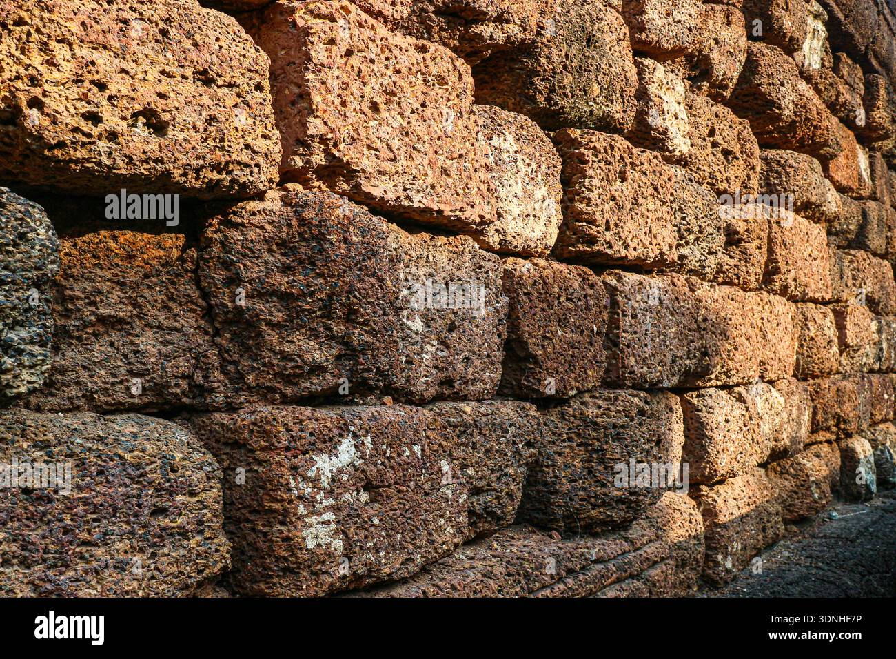 Perspektivische Ansicht einer alten Lateritwand mit starken Schatten. Ideal für historische Geschichten und archäologische Hintergründe. Stockfoto