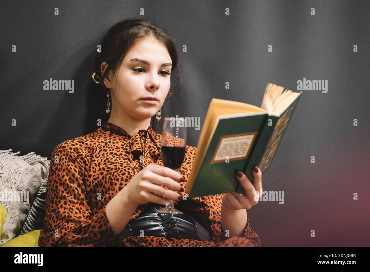 Dame mit Rotwein Glas Wein, das Buch im Hotelzimmer liest. Foto einer erwachsenen Frau, die Rotwein hält und drinnen Buch liest, Nahaufnahme. Stockfoto