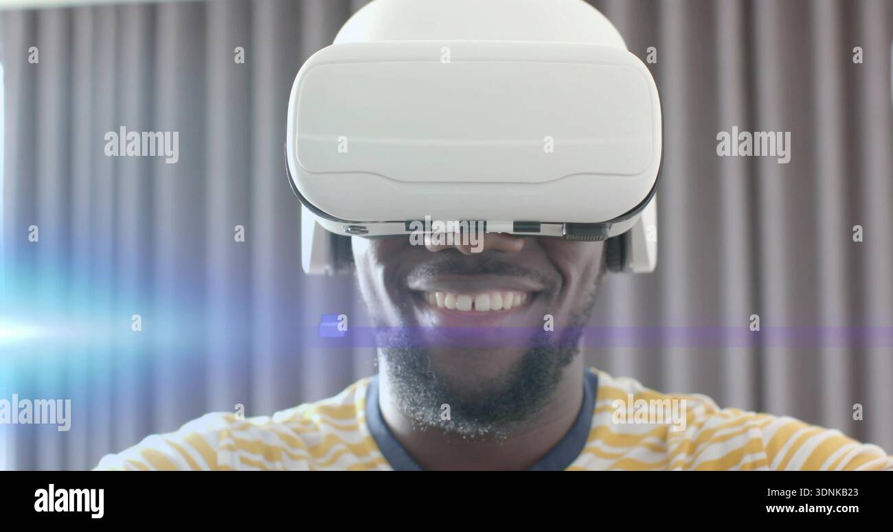 Lächelnder Mann mit weißem VR-Headset, das mit virtueller Szene zu Hause interagiert, gestreiftes T-Shirt Stockfoto