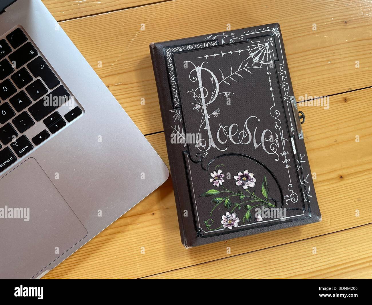 Traditionelles, handgefertigtes Poesie-Album „Poesie“ mit kunstvoller weißer Kreidedekoration und Blumen, neben einem modernen Laptop – analog vs. Digital Stockfoto