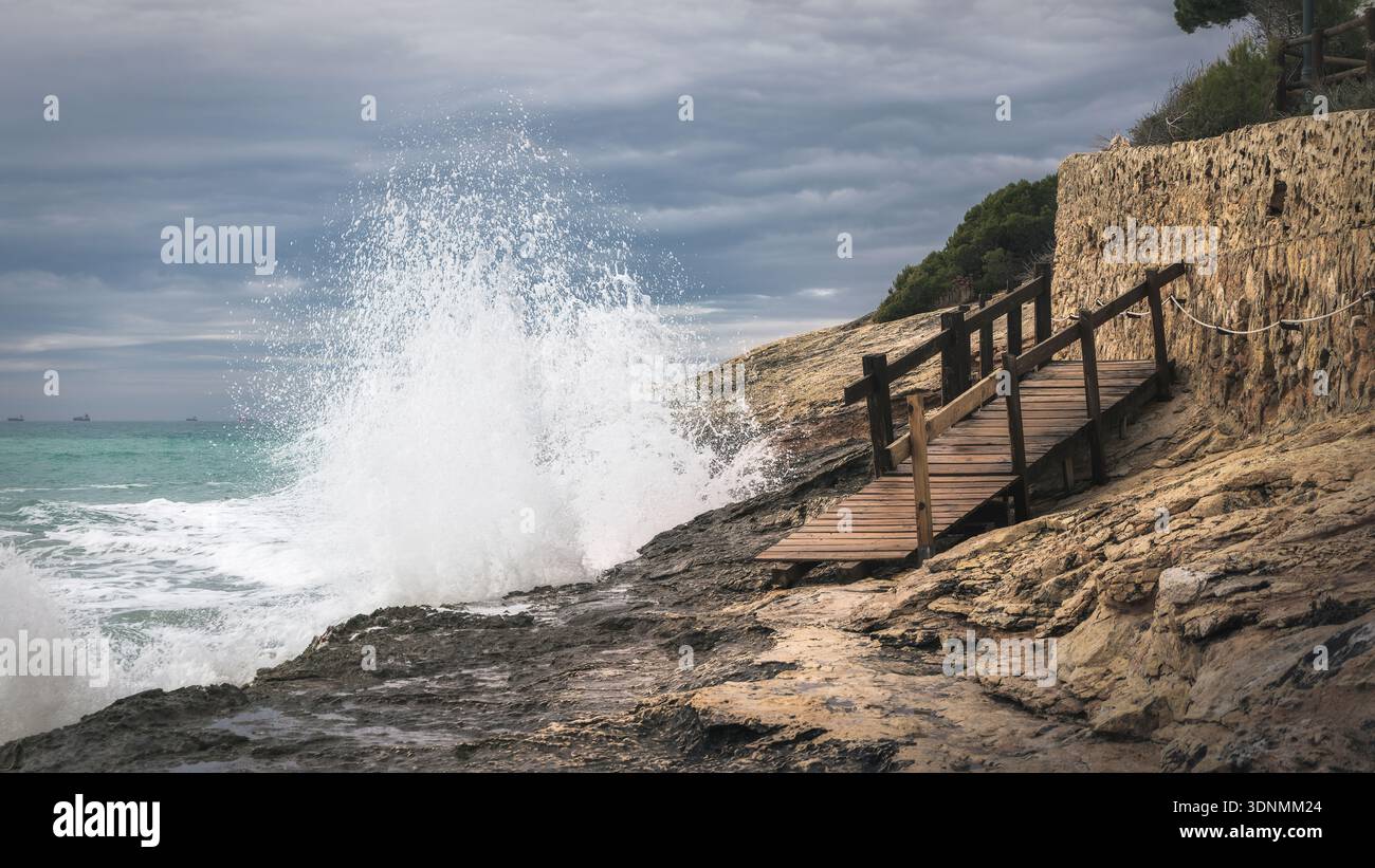 Wellen krachen gegen felsige Küsten, während Wolken den Himmel füllen, und schaffen eine dramatische Szene entlang der Cami de Ronda im farbenfrohen Torredembarra, Katalonien. Stockfoto