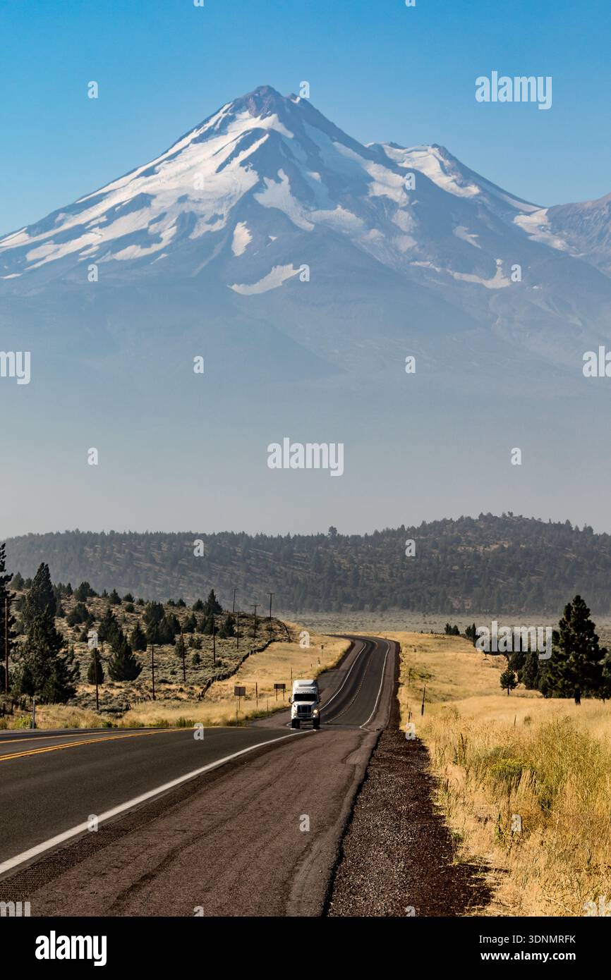 Der schneebedeckte Stratovulkan des Mount Shasta erhebt sich majestätisch über einem ländlichen nordkalifornischen Highway, dessen Gletscher bedeckt sind... Stockfoto