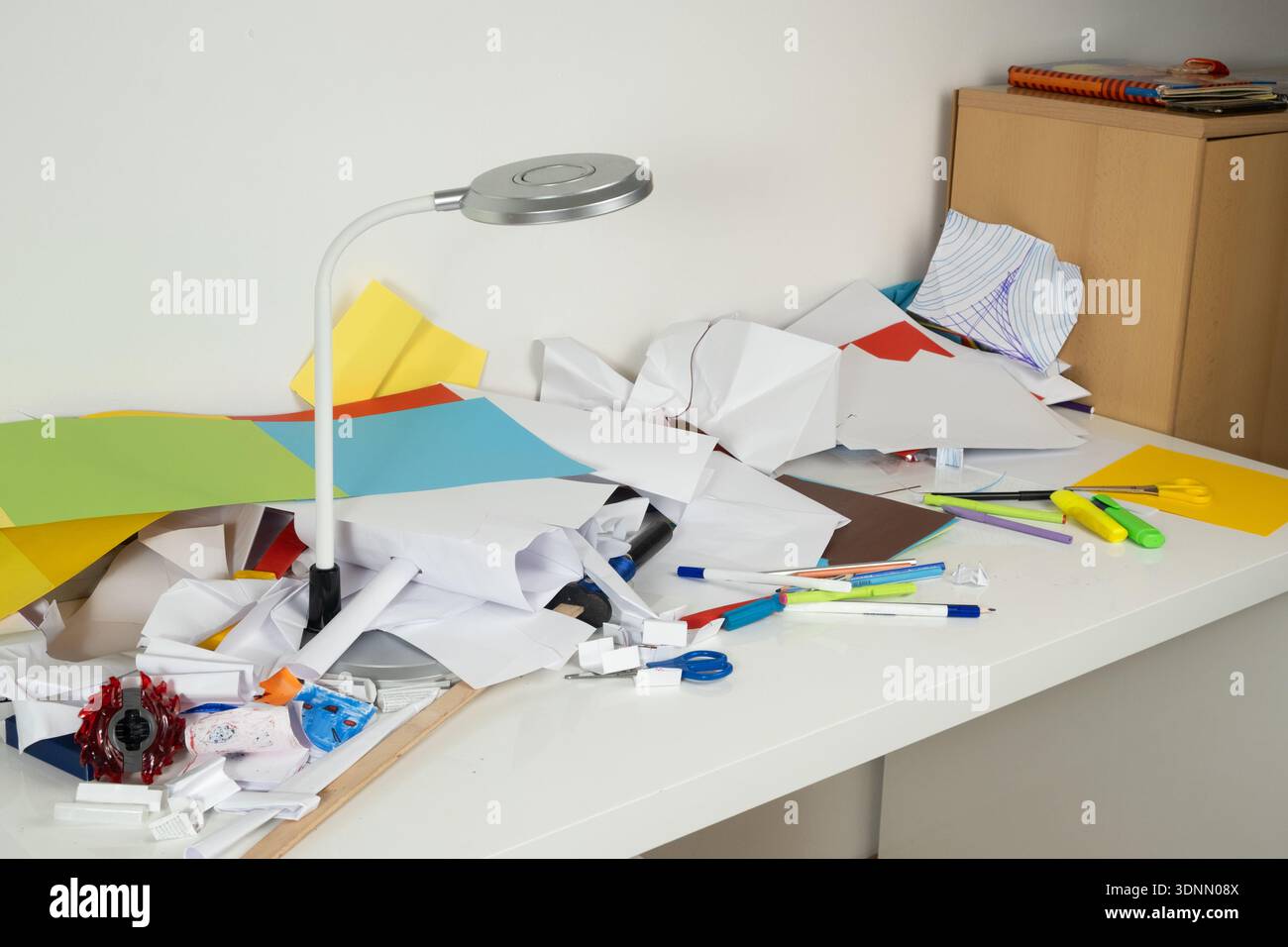 Zerknittertes Papier und unordentliche Schreibwaren auf weißem Schreibtisch unter der Lampe. Stockfoto