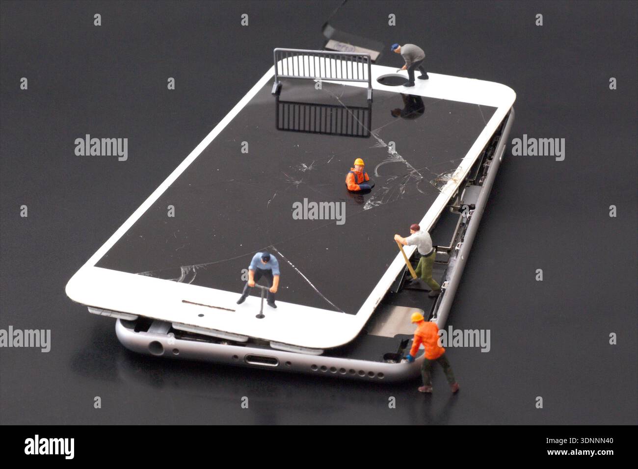 Miniaturfiguren zur Reparatur eines kaputten Smartphone-Bildschirms, die die Reparatur von Technologien veranschaulichen. Stockfoto