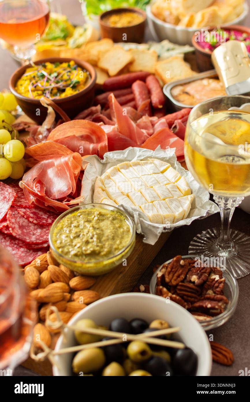 Versammelt um eine wunderschön gestaltete Wurstplatte gefüllt mit verschiedenen Käsesorten, köstlichen Würstchen, cremigem Hummus und frischen Trauben. Perfekt für kleine Treffen Stockfoto