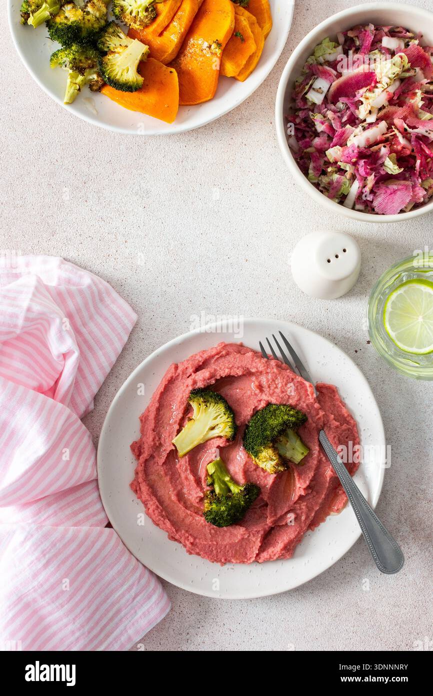 Ein gesundes Frühstück mit Rüben-Hummus, gebackener Süßkartoffel und Brokkoli, garniert mit frischem Rettich und Kohl Salat mit Protein und Nährstoffen Stockfoto