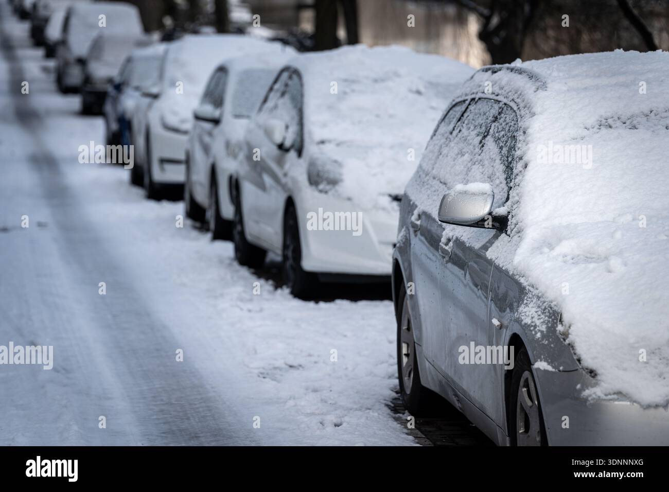 Eine Reihe schneebedeckter Autos parkte neben der vereisten Straße Stockfoto