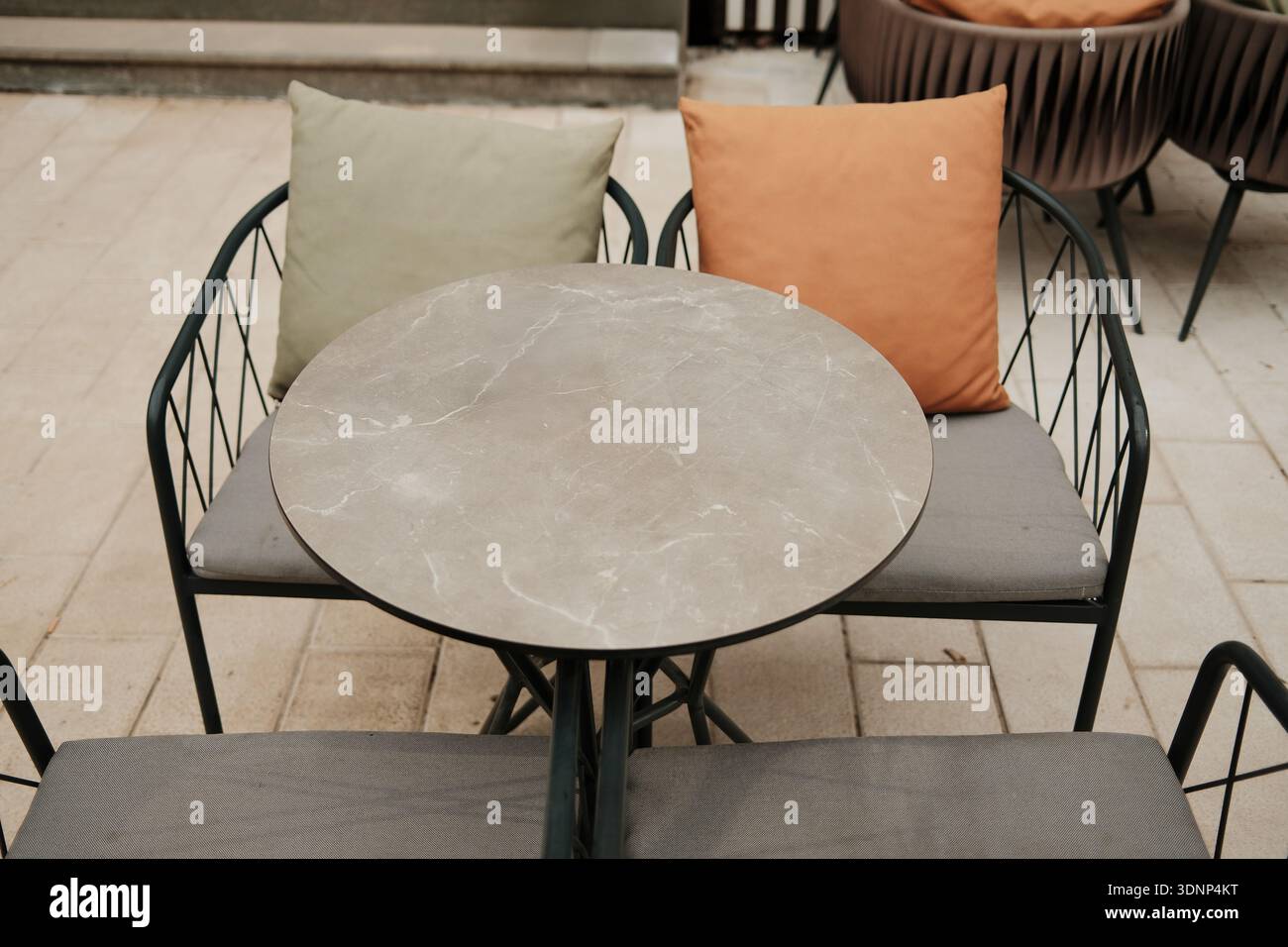 Runder Café-Tisch mit leeren Sitzen und weichen Kissen im Freien. Konzept der modernen Gastfreundschaft, minimalistisches Design, urbaner Komfort, lässig Stockfoto
