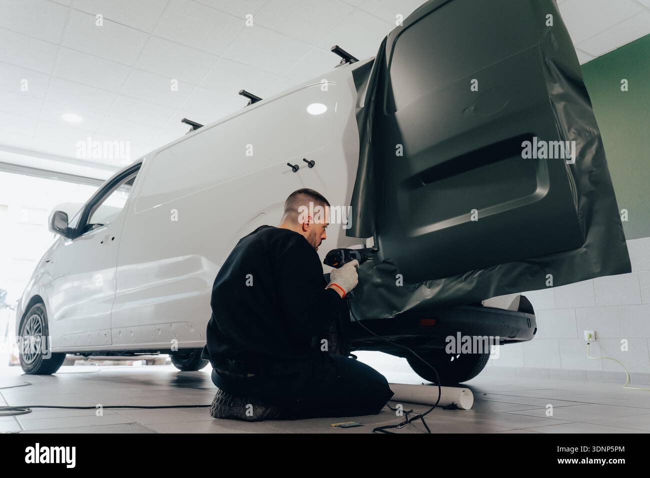 Ein professioneller Techniker arbeitet akribisch an einem Lieferwagen und trägt Vinylfolie für die automatische Anpassung auf. Dieser Prozess zeigt die Kunst der Fahrzeugmarke Stockfoto