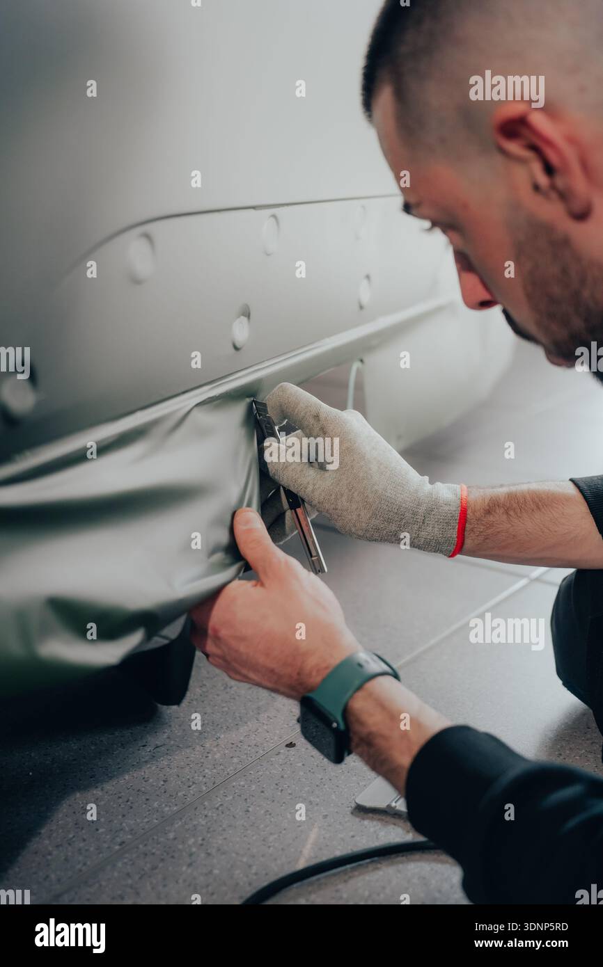 Ein erfahrener Techniker arbeitet akribisch an der Verpackung von Autos und zeigt handwerkliche Handwerkskunst bei der automatischen Anpassung in einer Automobilwerkstatt. Professionell Stockfoto
