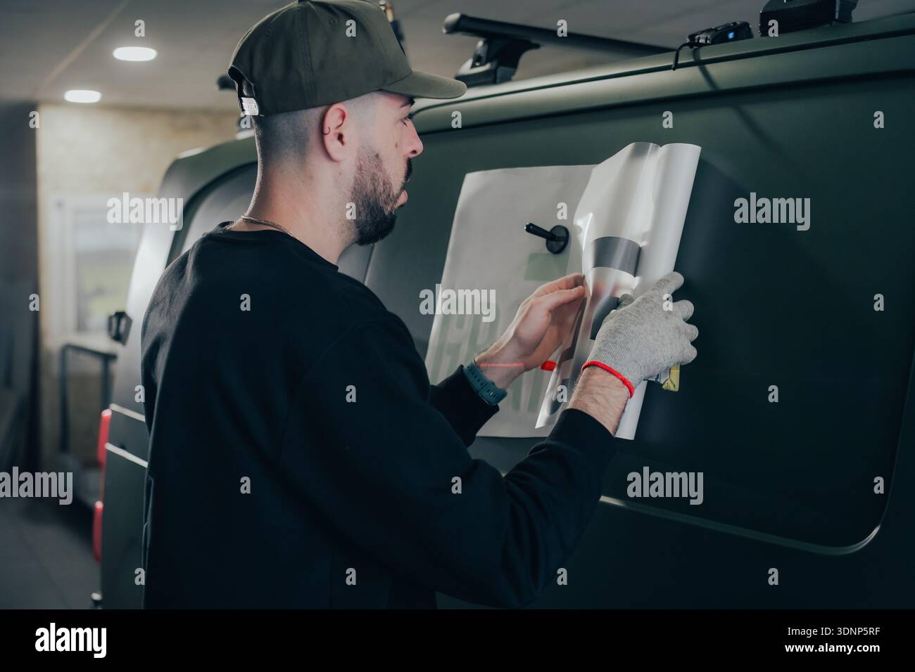 Ein erfahrener Mitarbeiter konzentriert sich auf die Vinylverpackung eines Fahrzeugs und zeigt den sorgfältigen Prozess des Verpackens und Brandings von Fahrzeugen. Dies unterstreicht die Kunst der Auto-Technik Stockfoto