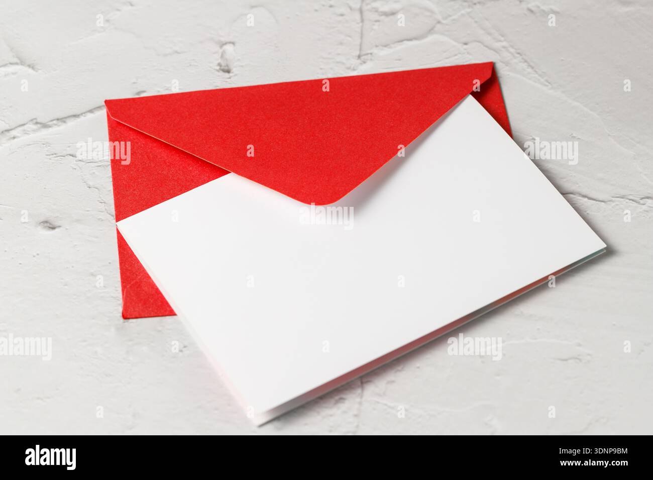 Roter Umschlag mit leerer Papierkarte Nahaufnahme auf hellem Betonsteinhintergrund. Mockup-Grußkarte mit Kopierraum Stockfoto