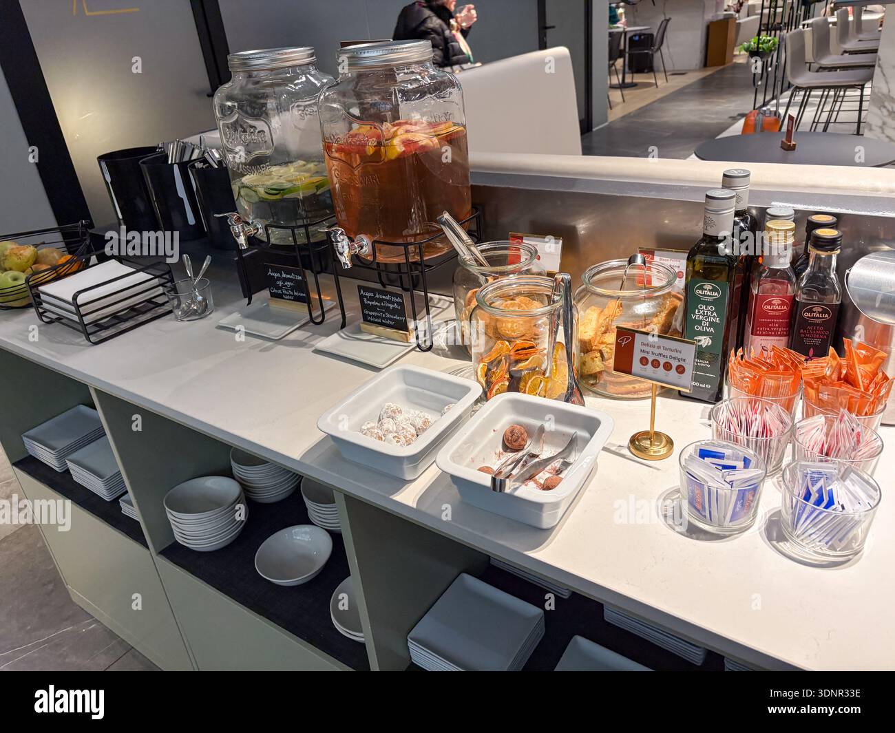Lounge-Bereich des Flughafens Rom Fiumicino (FCO) mit Selbstbedienungsbuffet mit Wasser, Keksen und italienischen Olivenöl. Reisereferenzen Stockfoto