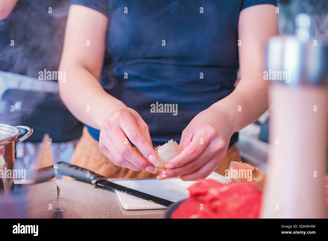 Frau mittleren Alters, die Zwiebeln hackt und sie in einen Topf mit kochendem Wasser gibt und selbstgemachtes Essen zubereitet Stockfoto